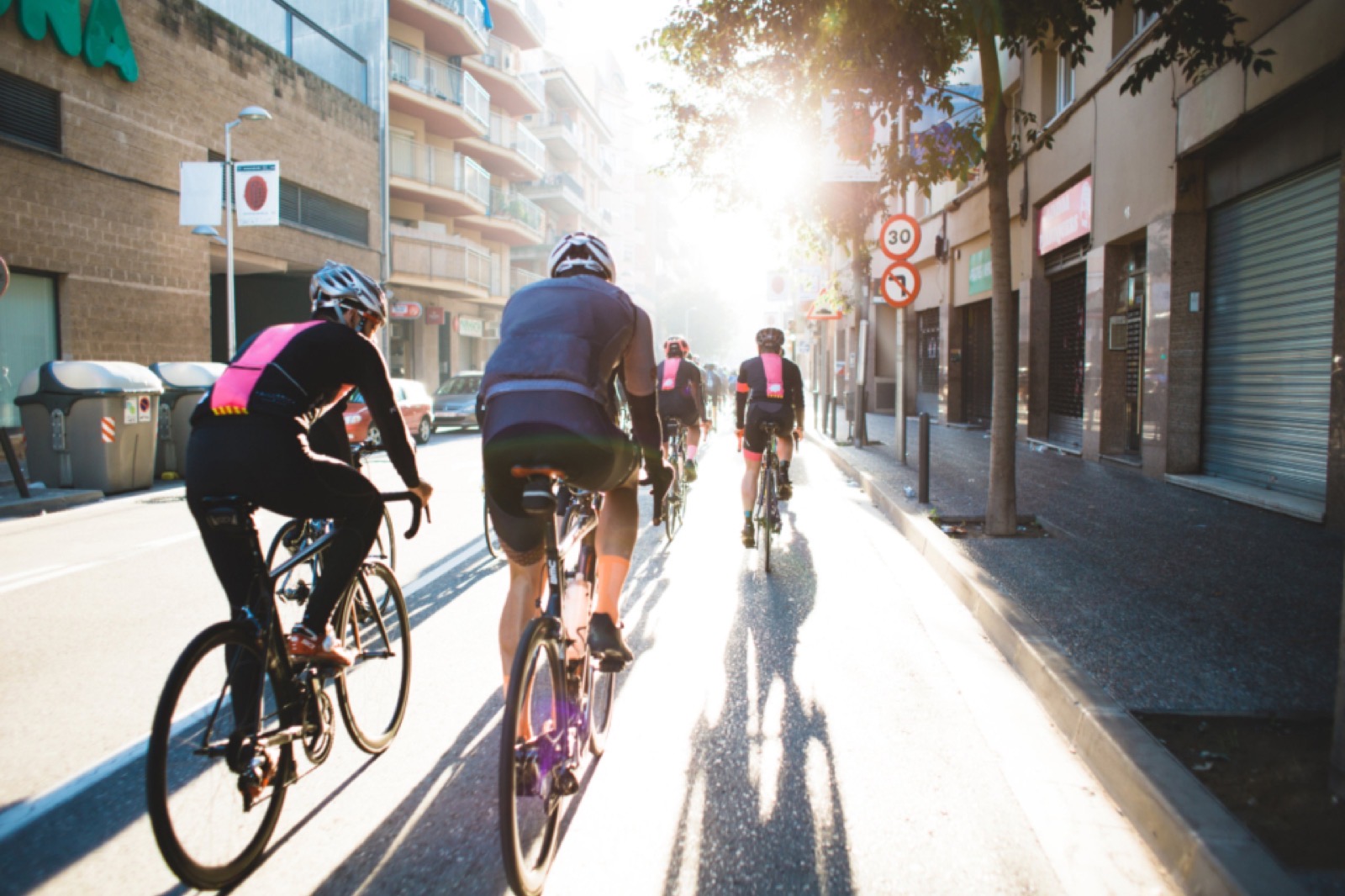 A group of road cyclists riding through a city street into backlit morning sun